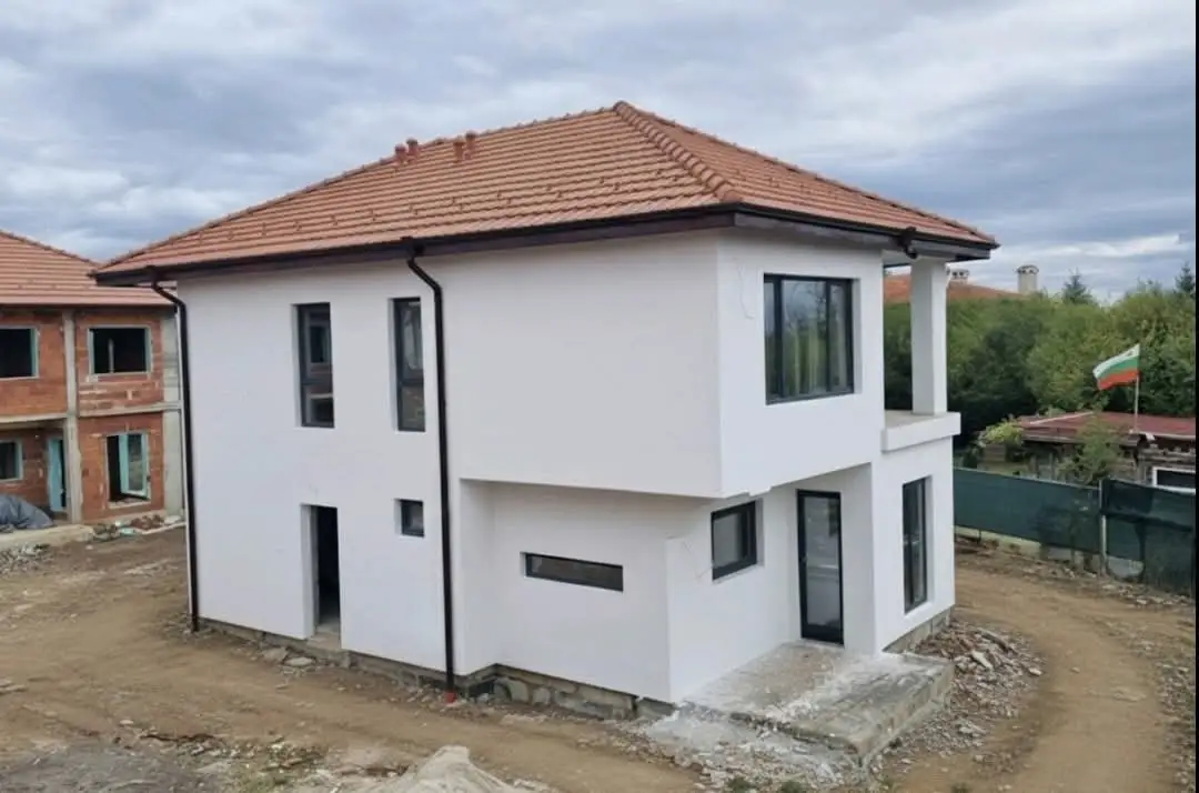 Новопостроена двуетажна бяла къща с модерен дизайн и керемиден покрив.