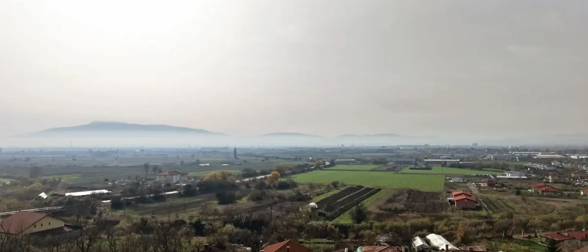 Панорамен изглед към равнина с ниви и планини в далечината.