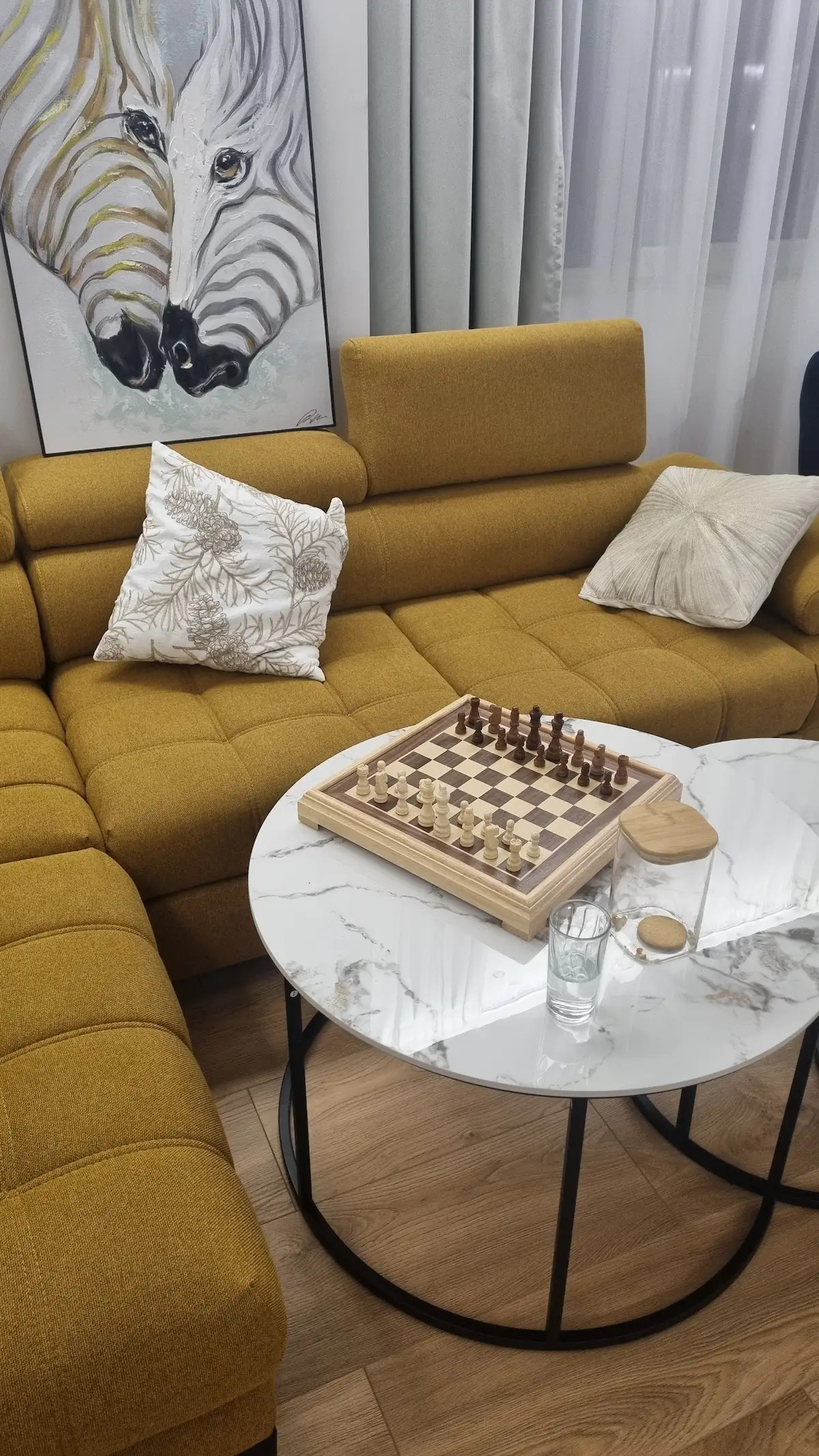 Интериор на хол с жълт диван, масичка с шах и картина на зебри.